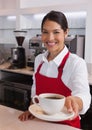 Pretty young barista offering cup of coffee smiling at camera Royalty Free Stock Photo