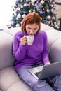 Pretty young beaming girl in a violet sweater drinking coffee