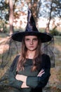 Pretty young beautiful woman in dark dress and witch hat standing in the middle of the autumn woods or park. Halloween Royalty Free Stock Photo