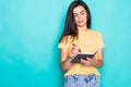 Pretty young beautiful woman standing, writing, take notes, holding textbook notebook organizer in hand and pen on turquoise Royalty Free Stock Photo