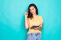 Pretty young beautiful woman standing, writing, take notes, holding textbook notebook organizer in hand and pen on turquoise Royalty Free Stock Photo