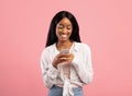 Pretty young black woman surfing web on smartphone on pink studio background