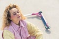 Pretty young blond ruddy woman sitting on the sports ground next to a pink scooter active free time concept eyes closed Royalty Free Stock Photo