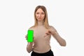 Pretty young blond woman is pointing thumb down and holds mobile phone with blank screen in her hand Royalty Free Stock Photo