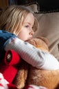 Pretty young blonde girl cuddling her teddy with her head on a cushion