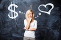 Pretty young blonde girl makes a choice between love and career. A woman chooses a heart or money. Heart and dollar sign drawn on Royalty Free Stock Photo