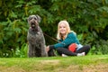 Pretty young blonde girl making eye contact while sitting on grass with well behaved black labradoodle dog on a leash Royalty Free Stock Photo