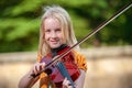 Pretty young blonde girl playing violin outdoors