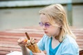 Pretty young blonde girl wearing purple sunglasses and enjoying a large ice cream with chocolate flake