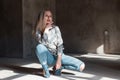 Pretty young blonde in a vintage stylish shirt in blue trendy ripped jeans in green trendy cowboy boots posing sitting Royalty Free Stock Photo
