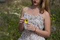Pretty young blonde woman defoliate a yellow daisy. The woman is wearing a dress with a flower pattern and is playing \