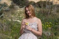 Pretty young blonde woman defoliate a yellow daisy. The woman is playing he loves m