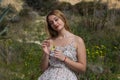 Pretty young blonde woman defoliate a yellow daisy. The woman is wearing a dress with a flower pattern and is playing he loves m