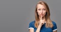 Pretty young blonde woman keeps finger on lips, making hush gesture on gray background. Shh, silence concept Royalty Free Stock Photo