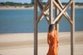 Pretty young blonde woman in orange dress leaning on the wooden lifeguard tower on the beach. The woman is nostalgic and sad. In