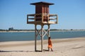 Pretty young blonde woman in orange dress leaning on the wooden lifeguard tower on the beach. The woman is nostalgic and sad. In