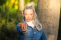 Pretty young blonde woman with a ponytail in her hair wearing a denim dress holds an orange in her hand and holds it out in front Royalty Free Stock Photo