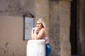 Pretty young blonde woman rests her face on her hands on a stone column. The wind moves her blonde hair