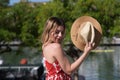 Pretty young blonde woman with straw hat and white dress with red print is having fun doing different poses with the hat close to Royalty Free Stock Photo