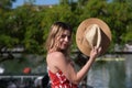 Pretty young blonde woman with straw hat and white dress with red print is having fun doing different poses with the hat close to Royalty Free Stock Photo