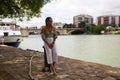 Pretty young blonde woman with sunglasses sitting on a river jetty. The woman looks nostalgic and lost in thought. Concept of Royalty Free Stock Photo