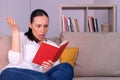 Pretty young brunette woman confused reading a book sitting on the sofa at home. Royalty Free Stock Photo