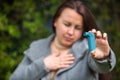 Pretty young brunette woman having asthma attack. She is holding inhaler. Asthmatic woman using an asthma inhaler during