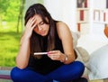 Pretty young brunette woman holding pregnancy home test, touching head with hand and looking depressed, bookshelves Royalty Free Stock Photo