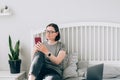 Pretty young brunette woman using mobile phone while working with laptop sitting on the bed at home Royalty Free Stock Photo