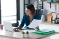 Pretty young business woman working with computer while consulting some invoices and documents in the kitchen at home Royalty Free Stock Photo