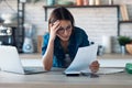 Pretty young business woman working with computer while consulting some invoices and documents in the kitchen at home Royalty Free Stock Photo