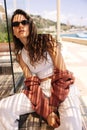 Pretty young caucasian girl in fashionable sunglasses sits on wooden bench near beach. Royalty Free Stock Photo