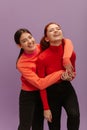 Pretty young caucasian girl hugging her sister standing in purple background. Royalty Free Stock Photo