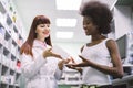 Pretty young Caucasian red haired pharmacist advising her young African female client at modern pharmacy how to take Royalty Free Stock Photo