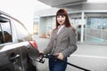 Pretty young Caucasian red haired woman, wearing denim jeans and jacket, filling her luxury car with petrol at gas Royalty Free Stock Photo