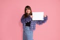 Pretty young dark-haired woman. Holds blank, clean, white sheet of paper for inscription smiles, looks into frame. Photo on pink Royalty Free Stock Photo