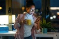 Pretty young entrepreneur woman using her smart phone while drinking a cup of coffee standing in the office