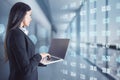 Pretty young european businesswoman typing on blank mock up screen laptop keyboard in blurry office interior with abstract glowing