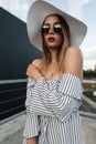 Pretty young fashionable woman in stylish sunglasses in trendy straw hat in elegant summer dress posing on street in city. Modern Royalty Free Stock Photo