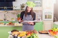 Pretty young female cook wearing Chef s hat looking for a recipe in cookbook standing in the kitchen Royalty Free Stock Photo