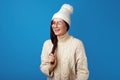 Cute girl smiles at camera, wears white hat and knitted white oversized sweater