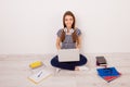 Pretty young female student in striped t-shirt, jeans and headphones sitting on the floor at home with laptop and books and Royalty Free Stock Photo