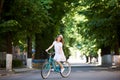 Pretty young female in white dress and straw hat riding blue bicycle middle of an empty green street Royalty Free Stock Photo