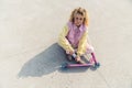 Pretty young fresh-faced blond woman sits on the ground pink scooter in front of her look at the camera full shot copy Royalty Free Stock Photo