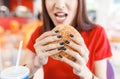 young funny woman eating hamburger inside in fast-food restaurant Royalty Free Stock Photo