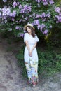 A pretty young girl, a beautiful woman in a blue long vintage dress is standing in a lilac garden. Summer, happiness, spring, warm