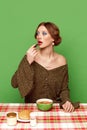 Pretty young girl with bright makeup eating vegetable soup against green studio background. Dinner time Royalty Free Stock Photo