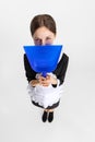 Pretty young girl in cleaning uniform hiding face behind dustpan isolated over white background