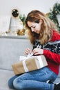 Pretty young girl opening presents near Christmas tree. Girl in red knitted sweater holds gift box Royalty Free Stock Photo