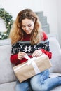 Pretty young girl opening presents near Christmas tree. Girl in red knitted sweater holds gift box Royalty Free Stock Photo